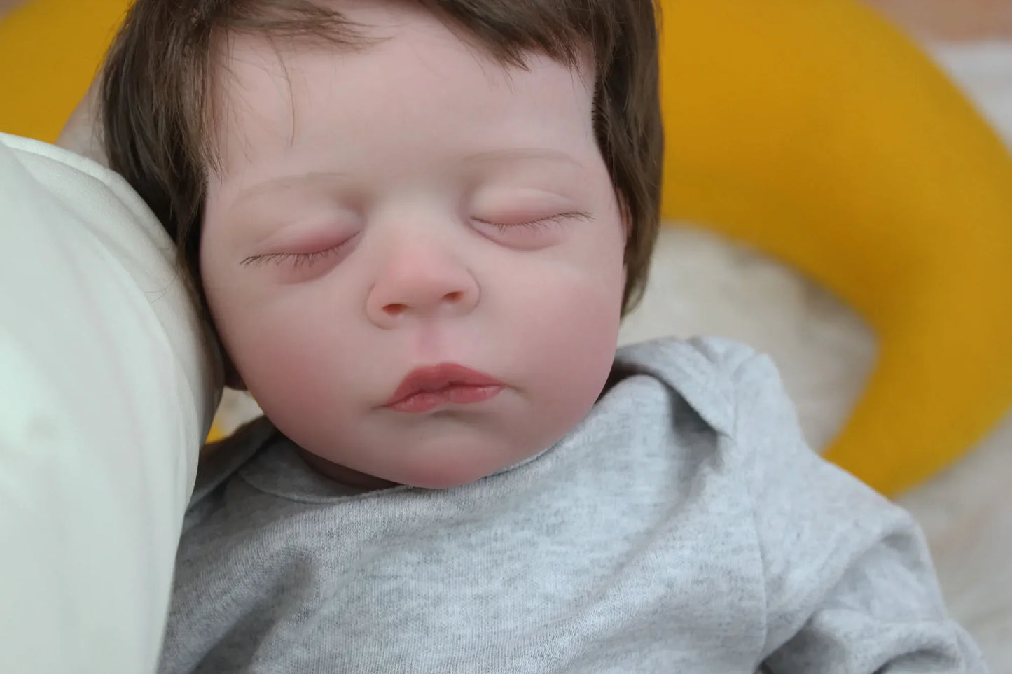 Lalka Reborn Lilli, realistyczne ciało z miękkiej tkaniny, ręcznie sadzone włosy i zamknięte oczy.