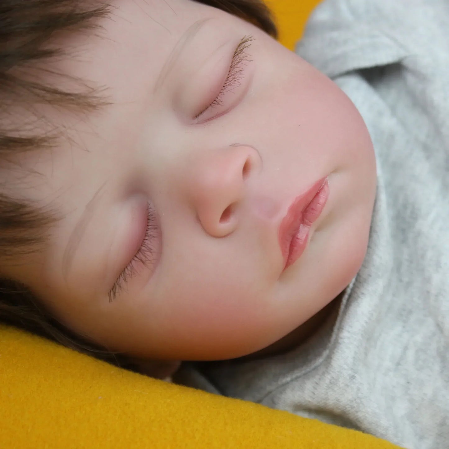 Lalka Reborn Lilli, realistyczne ciało z miękkiej tkaniny, ręcznie sadzone włosy i zamknięte oczy.